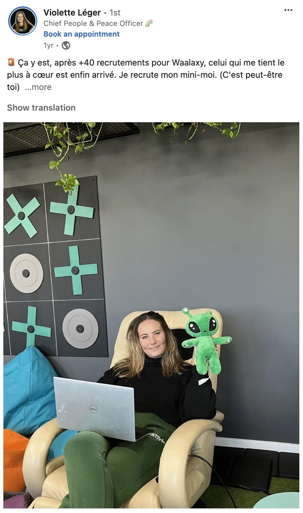 Femme assise en fauteuil avec ordinateur portable, jouet vert sur genoux, mur décoré de disques verts et plantes suspendues.